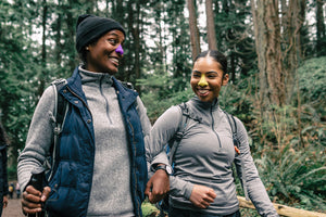 Two friends hiking a forest trail wearing Nöz reef safe, zinc oxide sunscreen in two neon shades.  